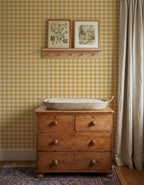 Okergeel Gingham-behang van Atelier Chien achter een houten commode met verschoonmand.