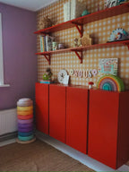 Okergeel ginghambehang van Atelier Chien achter een rode kast en wandplanken.